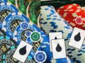 Pile of blue, green, and red poker chips with playing cards scattered on top in a colorful casino scene.